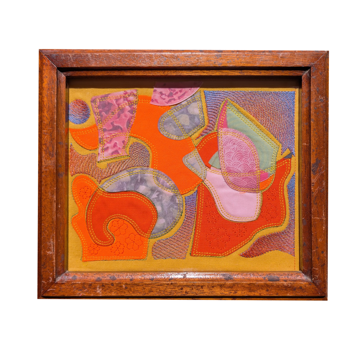 A framed abstract applique artwork featuring vibrant orange, pink, yellow, and purple stitched fabric shapes, enclosed in a rustic brown wooden frame against a solid white background.