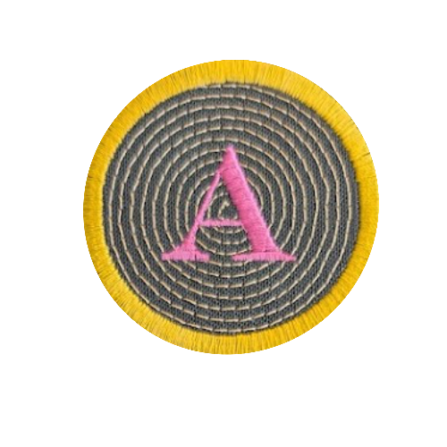 A circular embroidered patch featuring a yellow fringe border, a gray concentric spiral pattern, and a pink embroidered letter 'A' in the center, shown on a plain white background.