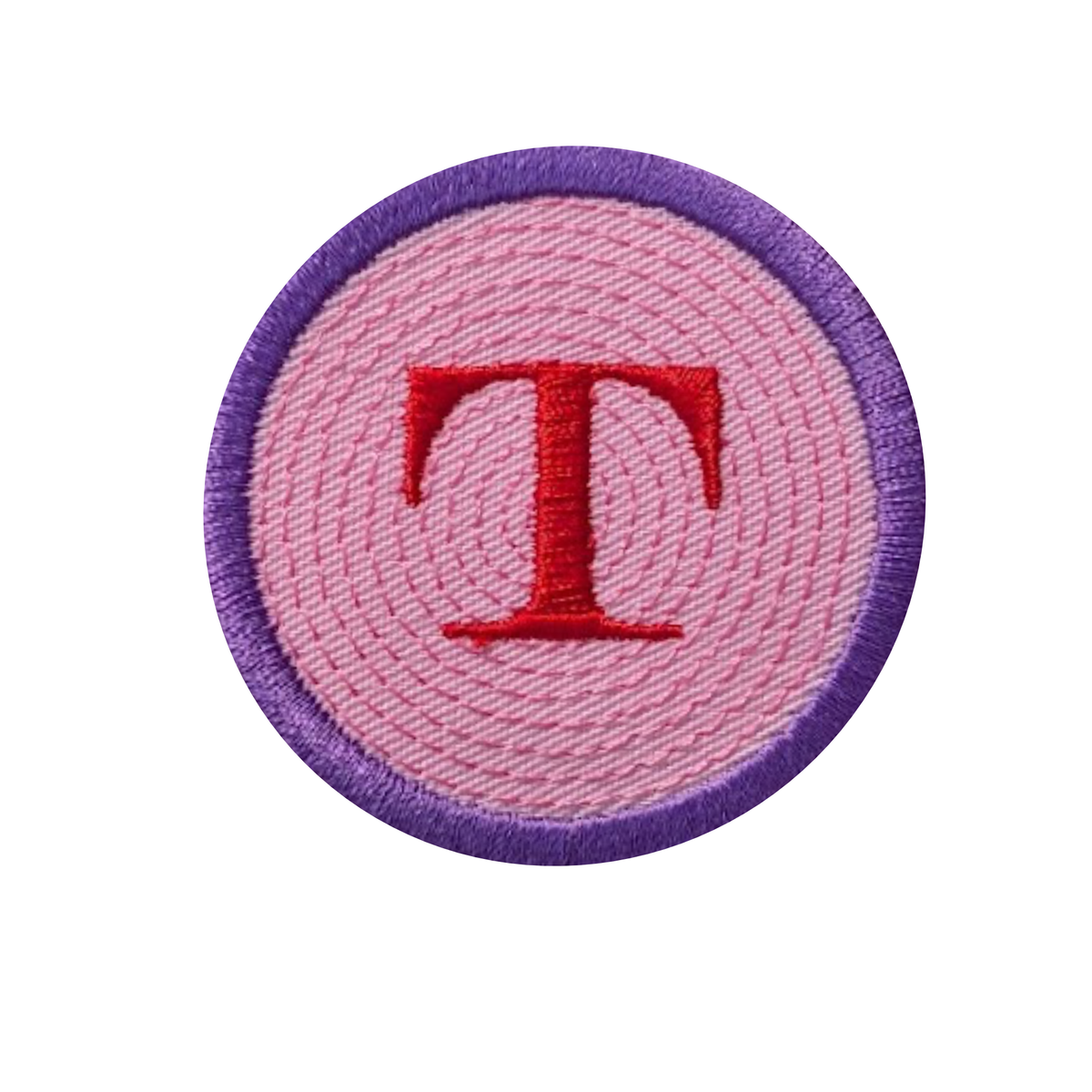 A circular embroidered patch featuring a textured pink background with a prominent red embroidered letter 'T' in the center, surrounded by a purple stitched border on a plain white background.